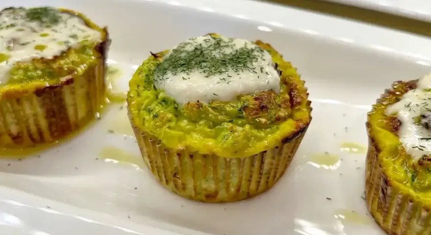 Tre tortini di zucchine dorati, guarniti con formaggio fuso e aneto, serviti su un piatto bianco.