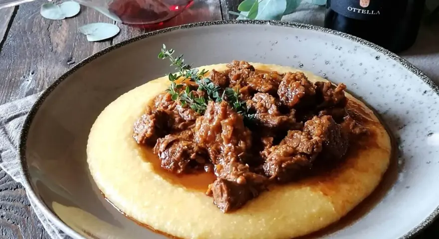 Un piatto di gulash con polenta fumante, guarnito con rametti di timo fresco. Un classico confortante, perfetto per una cena speciale.