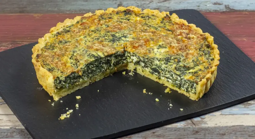 Una fetta di torta salata ricotta e spinaci, con crosta dorata e ripieno cremoso, su una lavagna scura.