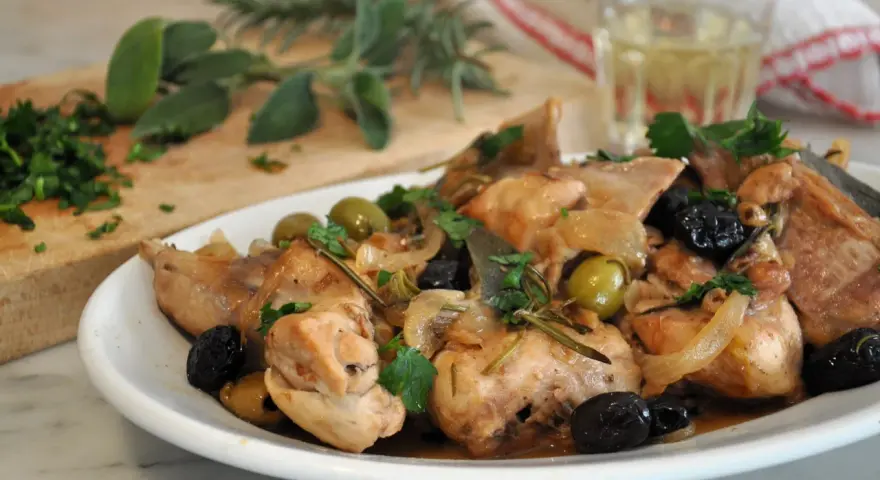Piatto di coniglio alla cacciatora in bianco, con olive verdi e nere, cipolle e rosmarino.