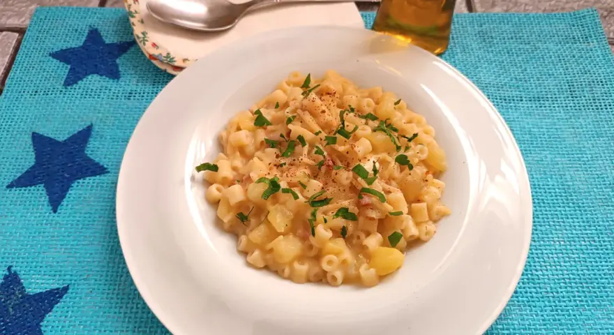 Un piatto di pasta patate e provola fumante, guarnito con prezzemolo fresco e un pizzico di peperoncino, pronto per essere gustato.