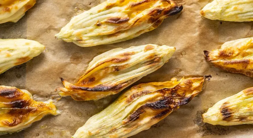 Fiori di zucca in pastella dorati e croccanti, appena sfornati su carta da forno.
