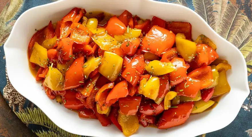 Peperoni in umido, colorati e succulenti, conditi con erbe aromatiche, serviti in una ciotola bianca su un tovagliolo decorato.