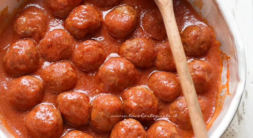 Succulente polpette di carne in un sugo rosso, pronte per essere gustate. Un cucchiaio di legno attende di servirle.