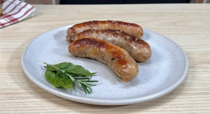 Tre salsicce dorate in padella, servite su un piatto con rosmarino e alloro.