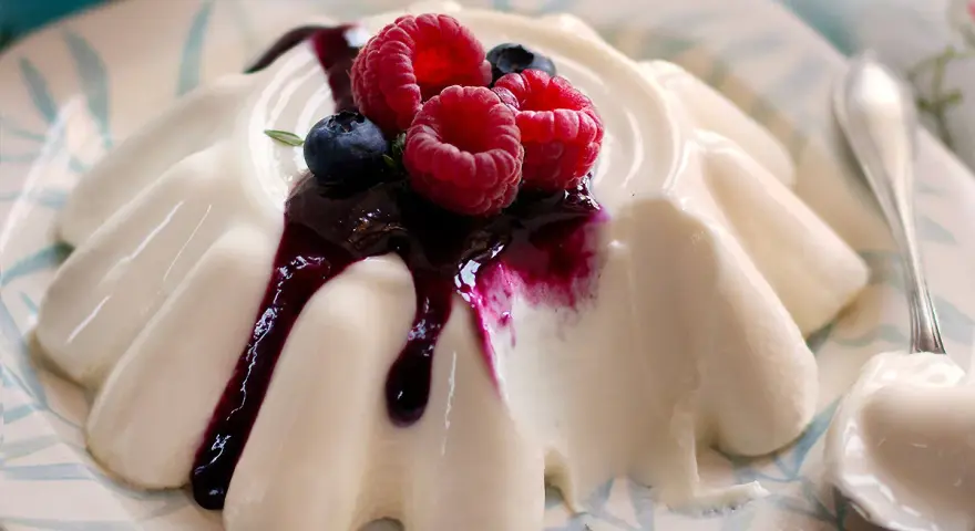 Deliziosa panna cotta con frutti di bosco e salsa ai mirtilli, servita su un piatto decorato.
