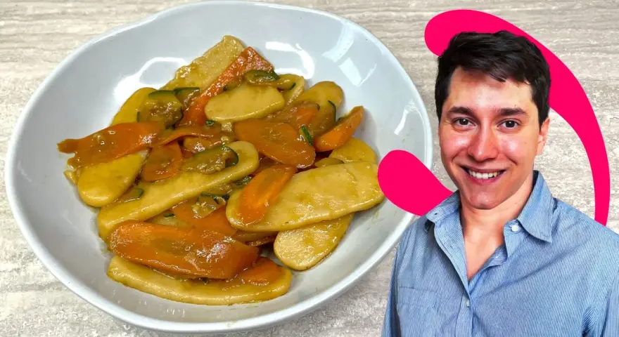 Un uomo sorride accanto a un piatto di gnocchi di riso con carote e zucchine.
