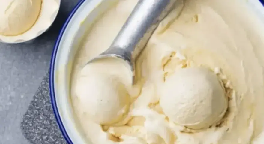 Un cucchiaio raccoglie una pallina cremosa di gelato fatto in casa, in una ciotola piena di delizia fredda.