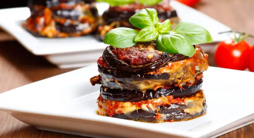 Parmigiana di melanzane, un classico della cucina italiana, servita su un piatto bianco con basilico fresco.