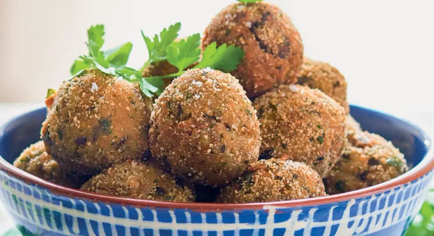 Polpette di melanzane dorate e croccanti, guarnite con prezzemolo fresco, in una ciotola blu decorata.
