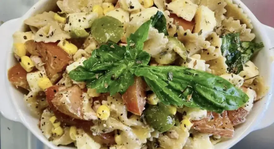 Un'insalata di pasta colorata con farfalle, pomodori, mais, olive verdi e basilico fresco, condita con erbe aromatiche.