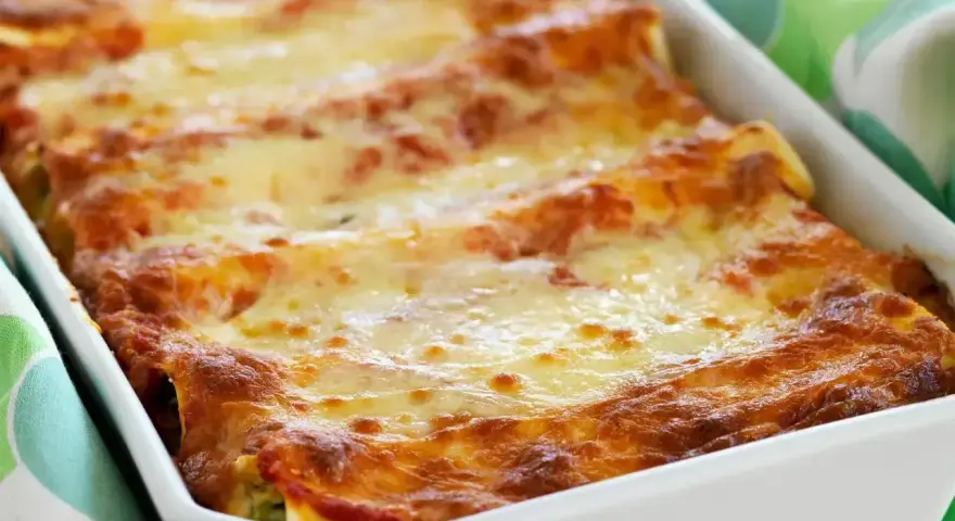 Cannelloni con ricotta appena sfornati, dorati e filanti, in una teglia bianca.