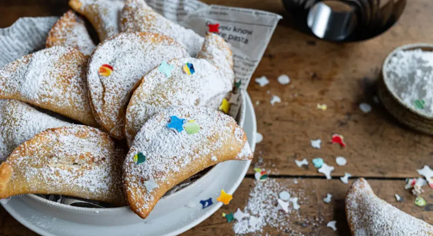 Cassatelle siciliane al forno, dolcetti dorati cosparsi di zucchero a velo e decorati con coriandoli colorati, pronti per essere gustati.