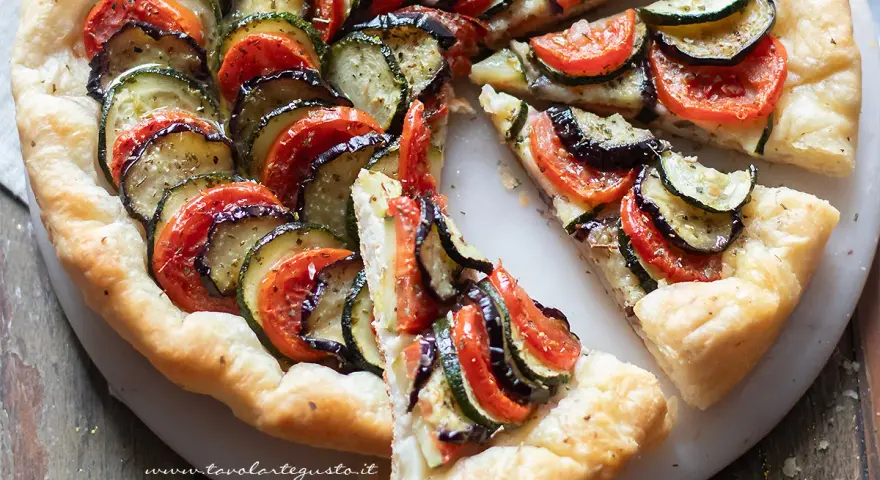Una deliziosa torta salata estiva con zucchine, melanzane e pomodori disposti a raggiera su una base croccante.