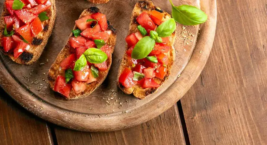 Bruschette veloci per aperitivo: fette di pane tostato con pomodoro fresco a cubetti e basilico, pronte per essere gustate.