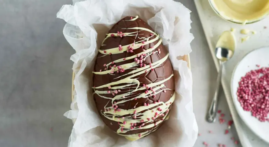 Un magnifico uovo di Pasqua fatto in casa, decorato con cioccolato bianco e granella rosa.