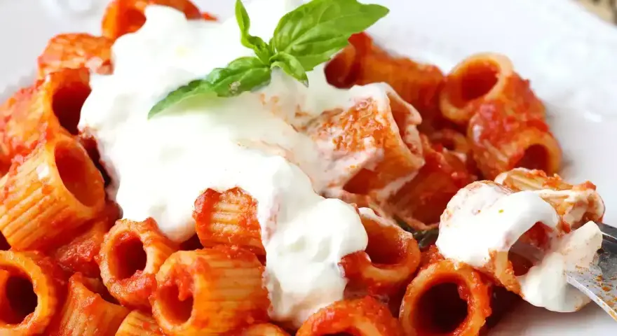 Rigatoni al sugo con abbondante stracciatella cremosa e una fogliolina di basilico fresco.
