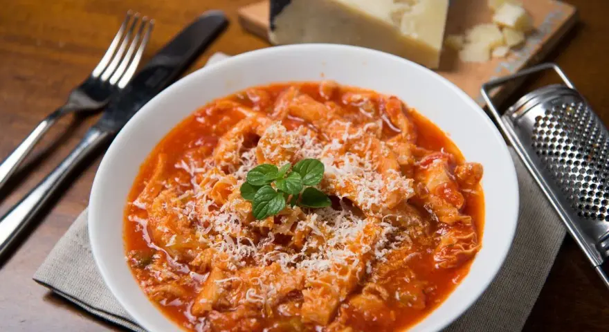 Un piatto fumante di trippa alla romana, cosparso di formaggio grattugiato e guarnito con menta fresca. Accanto, una grattugia e un pezzo di formaggio.