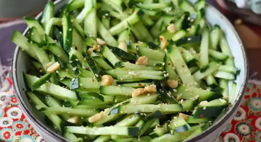 Una ciotola piena di fresca insalata di cetrioli tagliati a julienne, condita con semi di sesamo e arachidi croccanti.