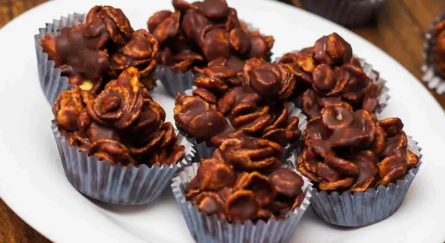 Deliziosi biscotti corn flakes e cioccolato, croccanti e golosi, serviti in pirottini argentati su un piatto bianco.