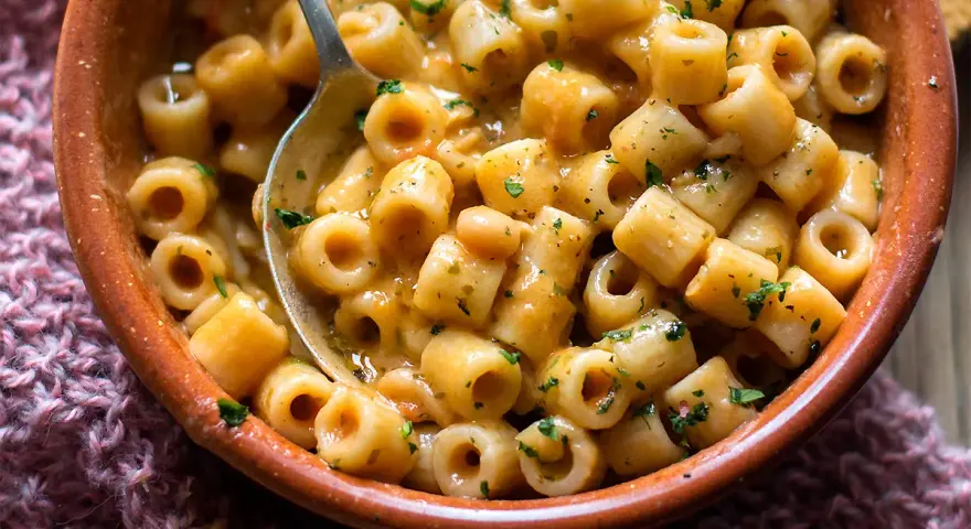 Un piatto invitante di pasta e fagioli estiva, condita con erbe fresche, servita in una ciotola di terracotta.