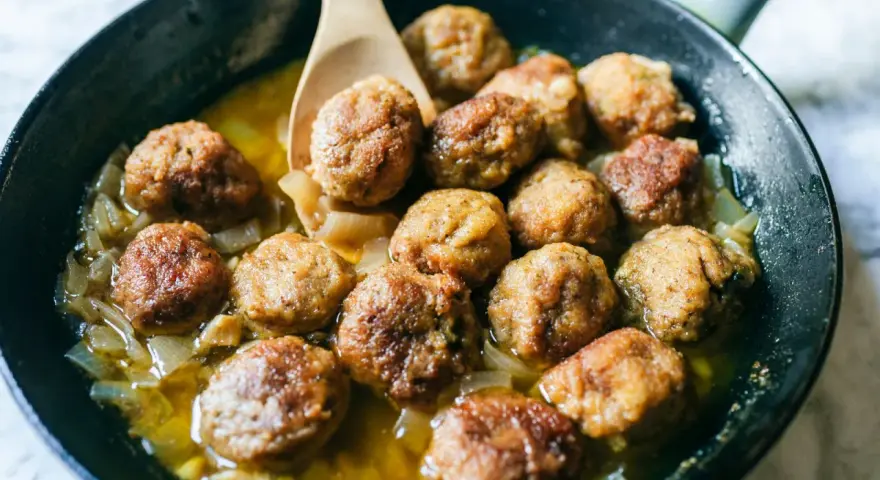 Polpette in bianco dorate e succulente, cotte in padella con cipolle dolci e un sughetto invitante. Un classico confortante.