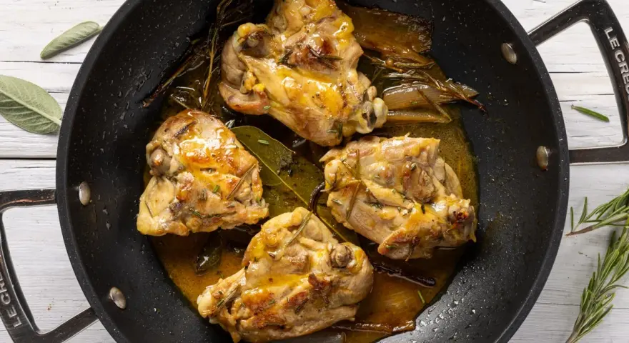Cosce di pollo in padella, dorate e succulente, con erbe aromatiche e un sughetto invitante.