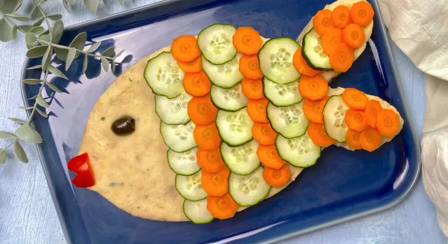 Un simpatico pesce finto ricetta, con corpo di purè, scaglie di cetriolo e carota, occhio d'oliva e bocca di peperone rosso.