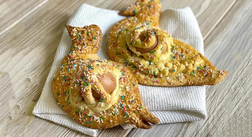 Due cuddure cu l'ova, dolci pasquali decorati con zuccherini colorati, riposano su un panno bianco.