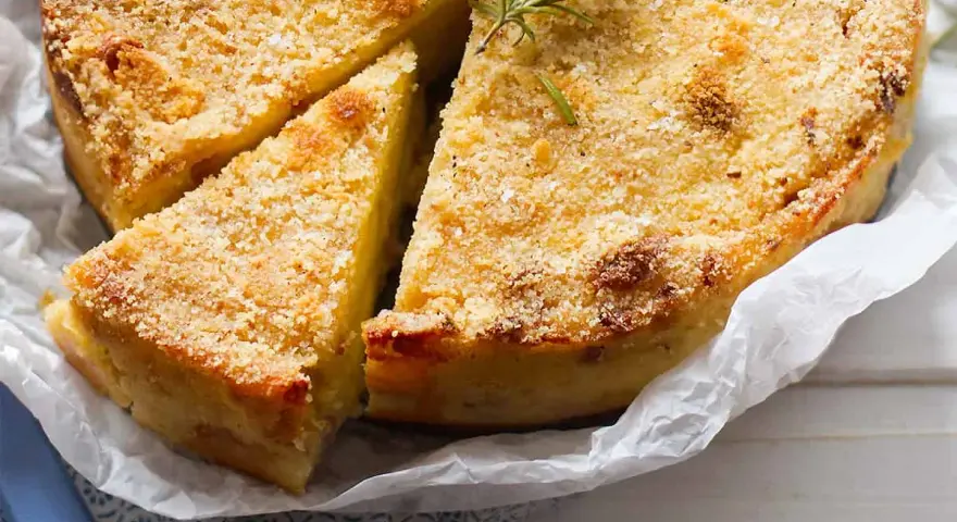 Gateau di patate alla siciliana dorato e croccante, guarnito con rosmarino fresco. Una fetta è già stata servita.