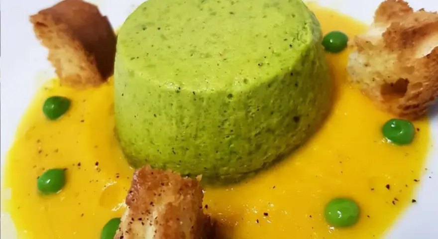 Sformato di piselli verde brillante su crema gialla, guarnito con piselli freschi e crostini dorati.