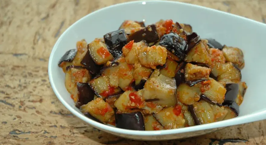 Melanzane al microonde, tagliate a cubetti e condite con pomodoro e spezie, servite in una ciotola bianca.