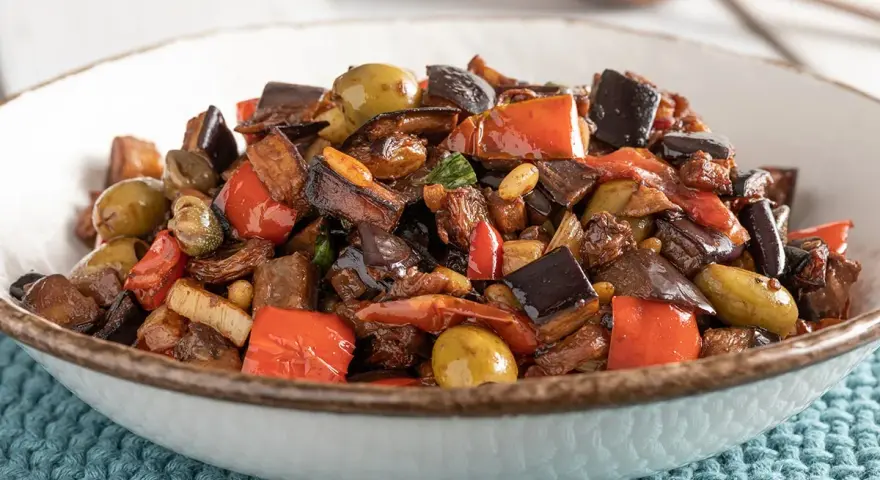Caponata ricetta: melanzane, peperoni, olive e capperi in un piatto invitante.