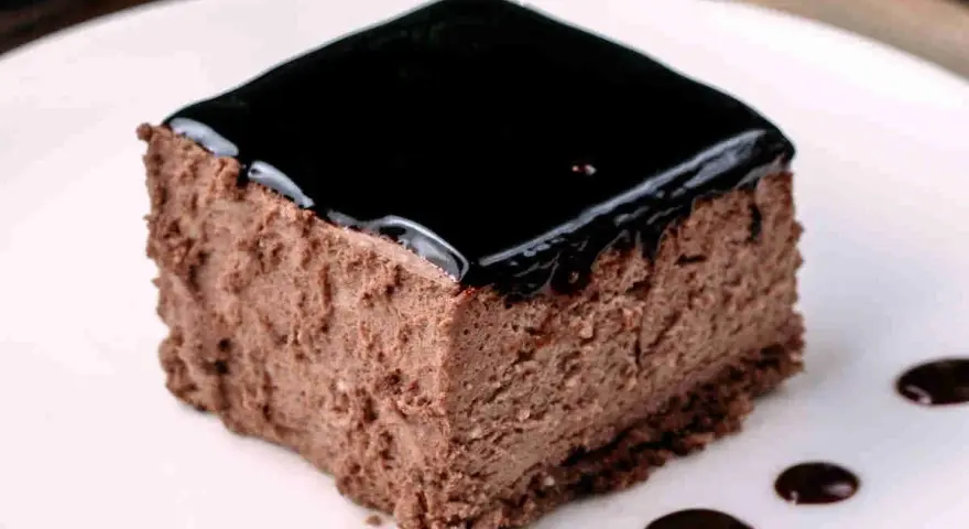 Un delizioso semifreddo al cioccolato, con una lucida glassa scura e gocce di salsa al cioccolato sul piatto bianco.