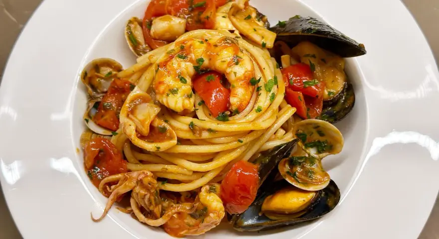 Un piatto invitante di spaghetti allo scoglio, con gamberi, cozze, vongole e calamari, condito con pomodorini freschi e prezzemolo.
