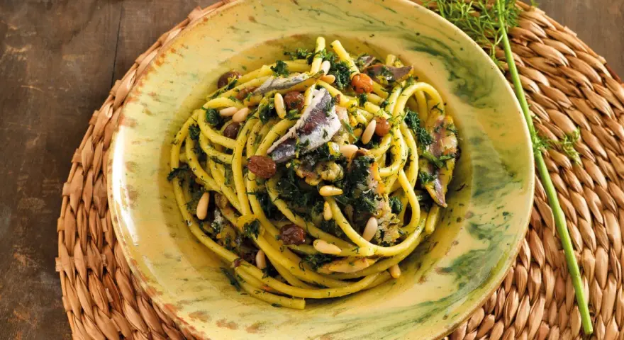 Un piatto di pasta con le sarde, condita con finocchietto selvatico, pinoli e uvetta, servita in un piatto decorato.