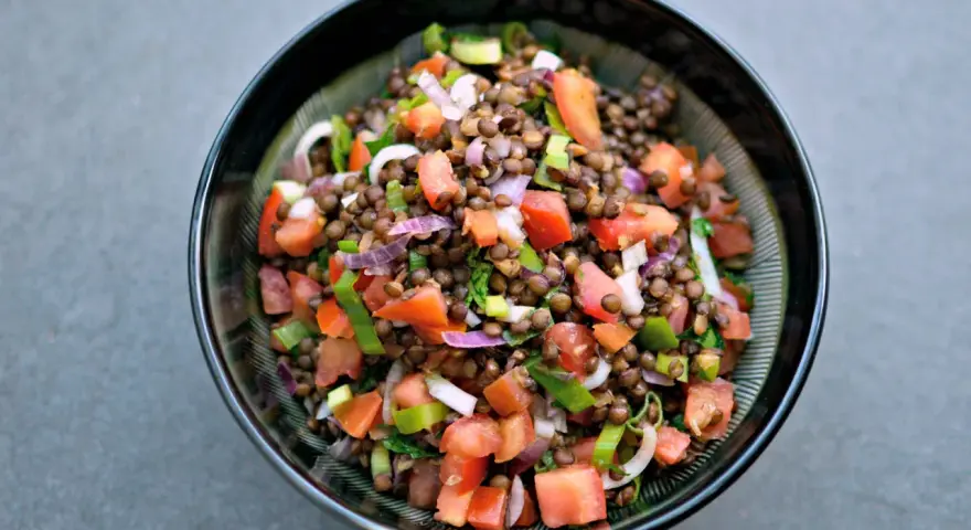 Una ciotola di insalata di lenticchie colorata con pomodori, cipolla rossa e erbe fresche.