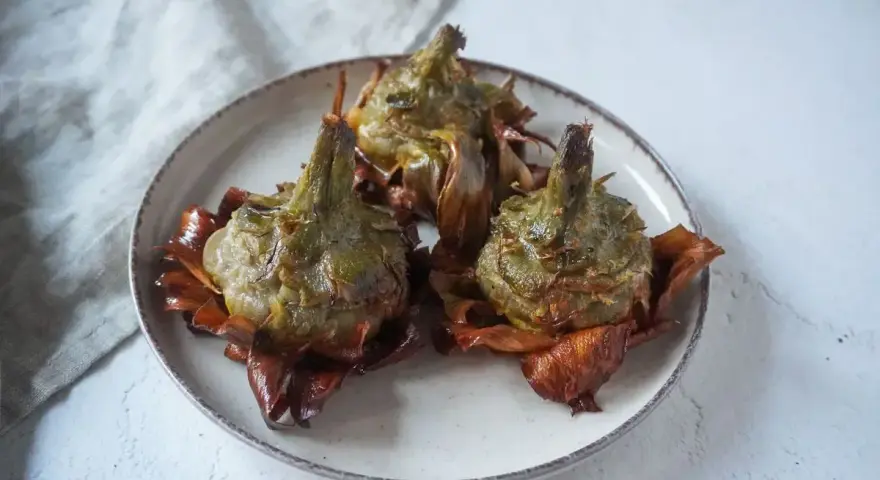 Tre carciofi alla giudia dorati e croccanti su un piatto, pronti per essere gustati.