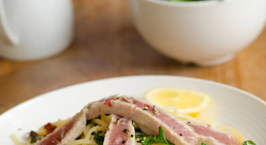 Spaghetti con tonno fresco alla siciliana, guarniti con rucola, capperi, pomodori secchi e una fetta di limone.