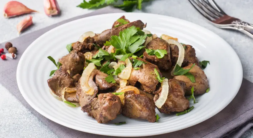 Piatto di fegato alla veneziana con cipolle e prezzemolo, contornato da aglio e pepe.