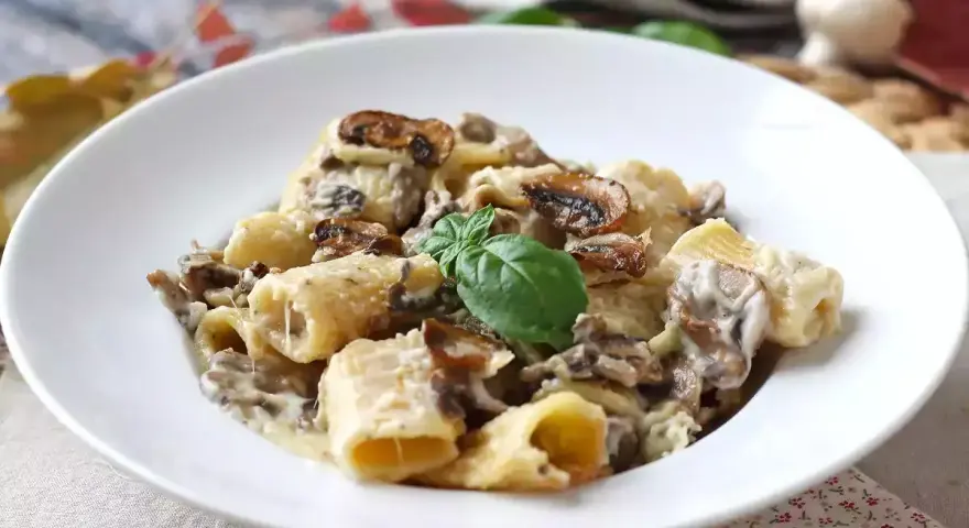 Un piatto invitante di pasta funghi e panna, con rigatoni conditi generosamente e guarniti con basilico fresco.