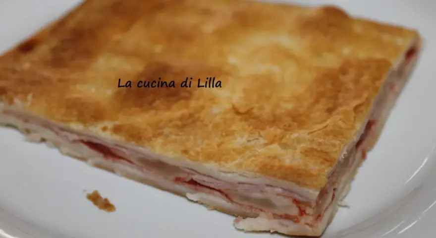 Una fetta di torta salata prosciutto e formaggio, con pasta sfoglia dorata e ripieno filante.