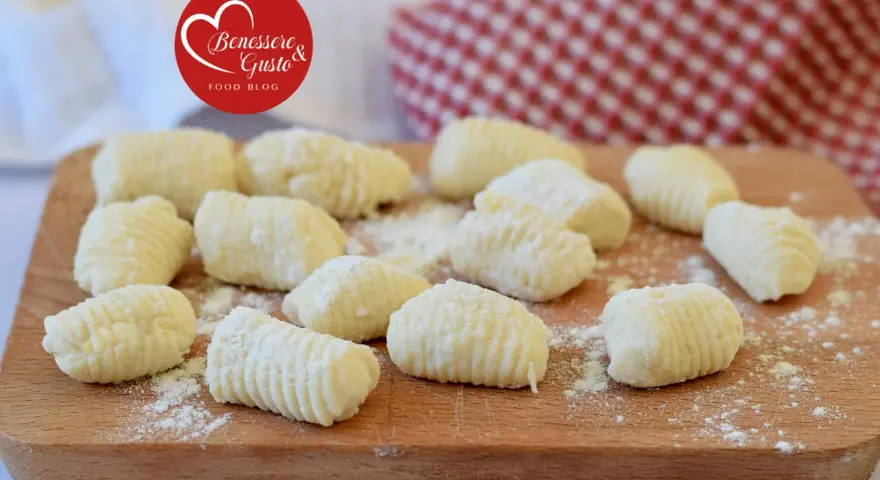 Gnocchi di ricotta freschi, pronti per essere cucinati, spolverati di farina su un tagliere di legno.