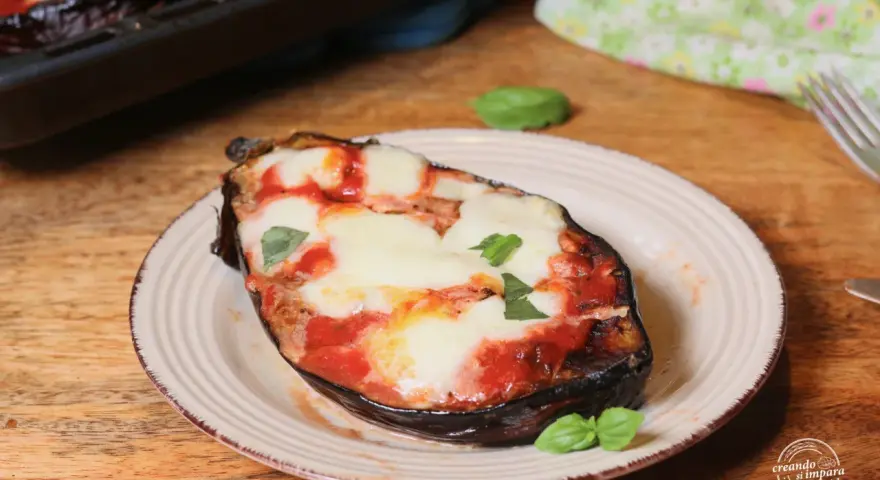 Melanzane alla pizzaiola appena sfornate, con mozzarella filante e basilico fresco su un piatto rustico.