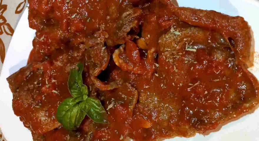 Fette di carne alla pizzaiola, ricoperte da un sugo rosso saporito e guarnite con basilico fresco.