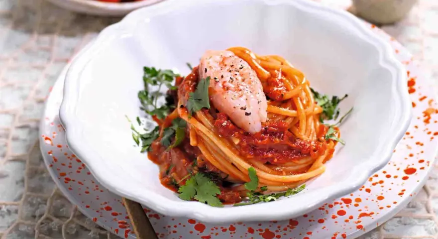 Spaghetti con gamberetti e pomodorini alla siciliana, un piatto colorato e saporito, guarnito con prezzemolo fresco.