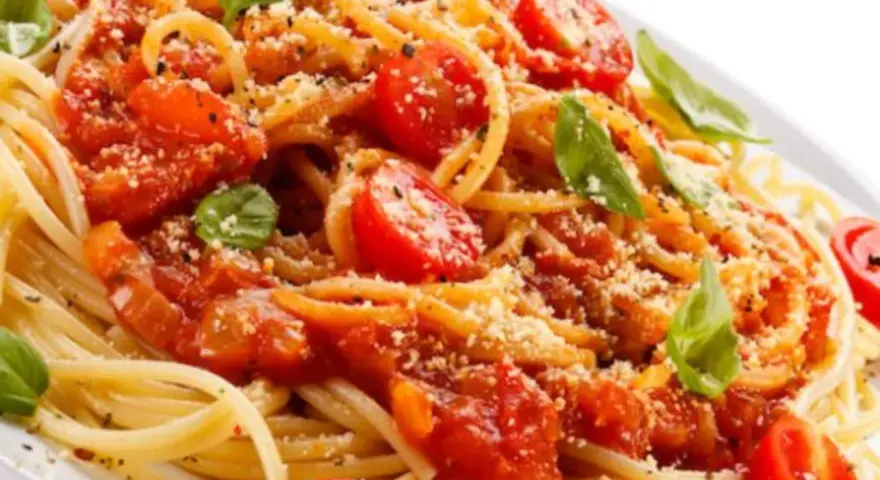 Un piatto di spaghetti alla carrettiera, conditi con pomodoro fresco, basilico e parmigiano grattugiato.