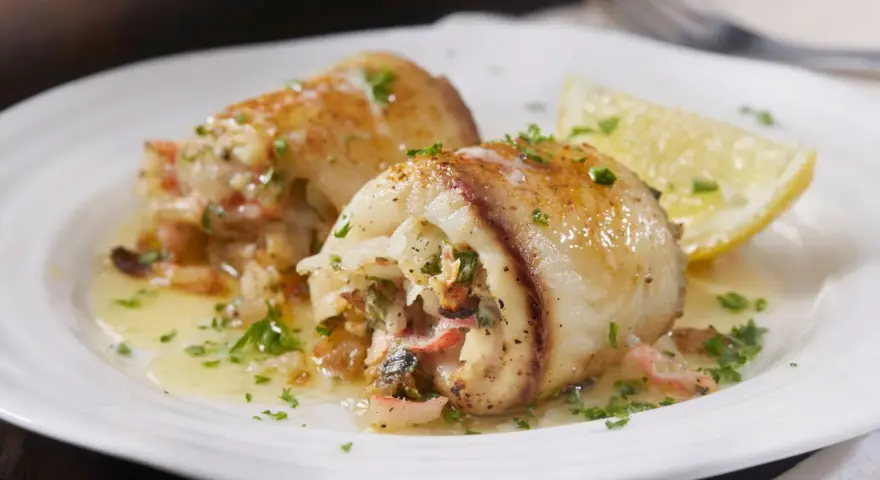 Deliziosi involtini di pesce spada ripieni, serviti su un piatto bianco con spicchio di limone e prezzemolo tritato.