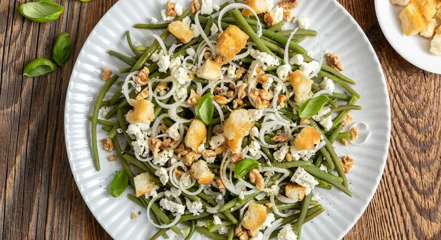 Deliziosa insalata di fagiolini con formaggio feta, noci croccanti, crostini e cipolla rossa. Un piatto fresco e saporito.