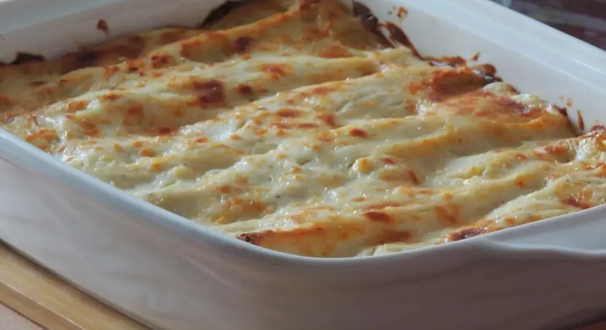 Lasagne con carciofi, besciamella e mozzarella appena sfornate, dorate e filanti in una teglia bianca.